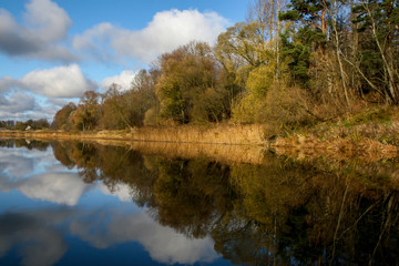 Autumn landscape with colorful trees, yellow grass and river. Reflection in river