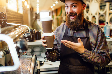 Excited young barista points on two cups of coffee stand one upon another. He looks on camera and smiles. Guy stand in kitchen close to coffee machine.