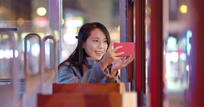 Woman take photo on cellphone on the tram at night