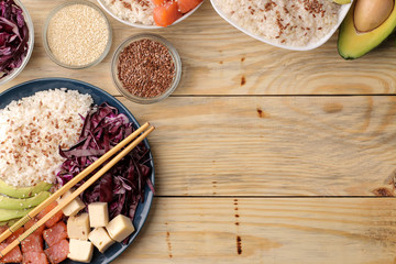 poke bowl Hawaiian food. a plate of rice, salmon, avocado, cabbage and cheese. next to sesame seeds on a natural wooden table top view. with space for text