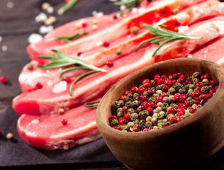 Raw beef steak on a cutting board with rosemary and spices.