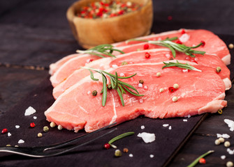 Raw beef steak on a cutting board with rosemary and spices.