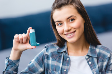 happy young woman holding inhaler and smiling at camera
