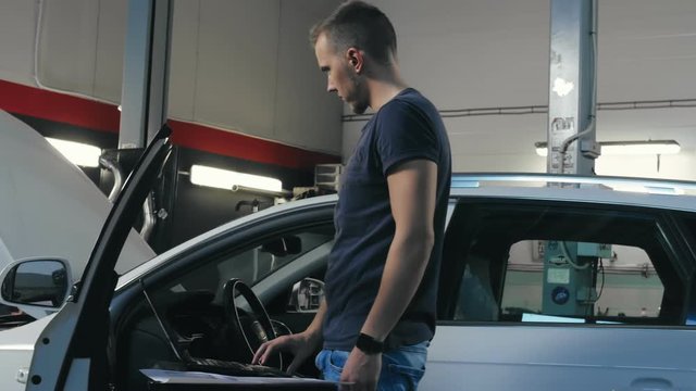 Technician man making computer diagnostics car engine in repair shop