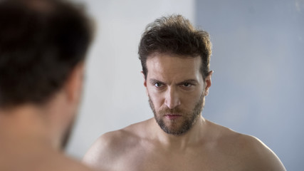 Obraz premium Man looking at his mirror reflection with hatred and shame, feeling guilty