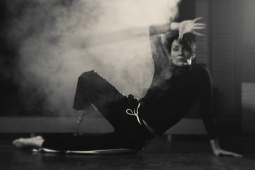 modern beautiful dancer in black clothes posing against the Studio in the smoke
