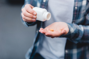 cropped shot of woman holding container and taking medicine at home