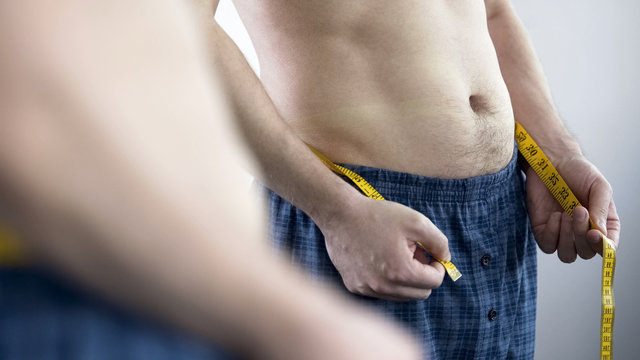 Man in home clothes measuring volume of his hips after debilitating diet