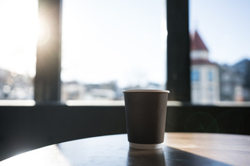 Isolated coffee in paper cup setting on wood teak table in cafe with natural light through the window/ Morning time /space for advertising / standalone cup /close up object with background /