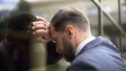 Pensive male leaning on office wall, work failure problem, disappointment