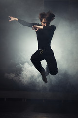 Fototapeta na wymiar modern beautiful dancer in black clothes posing against the Studio in the smoke
