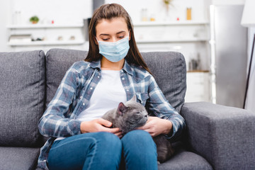 girl in medical mask holding cat and suffering from allergy at home