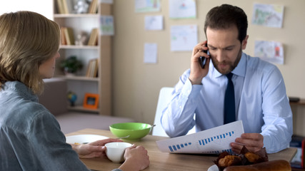 Busy husband in suit discussing company statistics on cellphone, ignoring wife