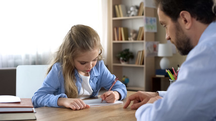 Fototapeta na wymiar Diligent female preschooler doing homework with caring father, education
