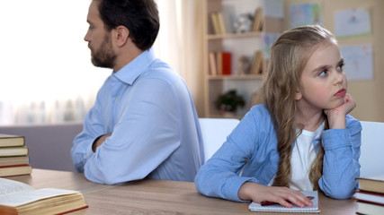 Stubborn father and daughter sitting at table keeping silent, conflict in family