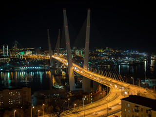 Fototapeta na wymiar Zolotoy most or Golden Bridge, Vladivostok, Primorsky region, Russia. The lights of the night city under a cable-stayed bridge over the river with construction cranes on the shore. December, 2018