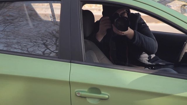 A private detective or a spy conducts surveillance of the object of surveillance. A man secretly taking pictures from the car window