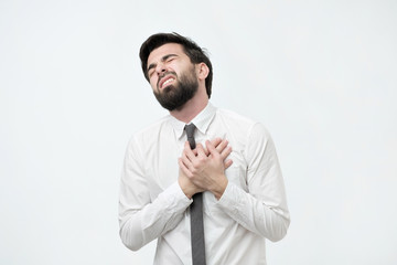 Naklejka premium Young spanish bearded man having heart attack on white background. Having health problem because of hard working lifestyle.