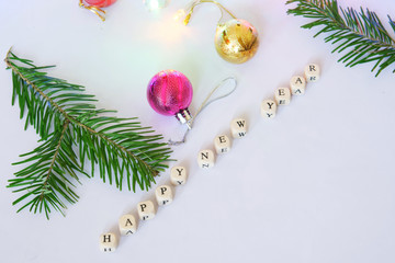 Happy New Year. Cubes with letters on a light surface together with a branch of a Christmas tree and Christmas toys