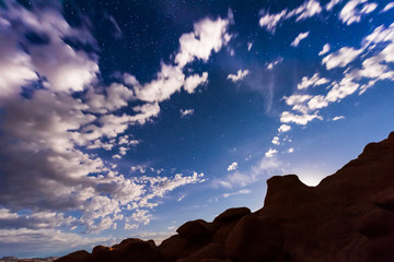 Night sky with full moon rising, or moonrise, in Goblin Valley State Park in Utah showing clouds, stars, and canyons silhouettes in wilderness nature