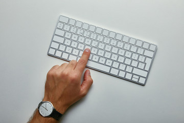 Cropped view of man pushing button on computer keyboard on grey background