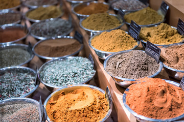 Many spices on display in bowls trays filled with herbs, signs, garam masala, paprika, turmeric, mixes