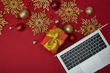 Top view of laptop near wrapped present and decorations on red background