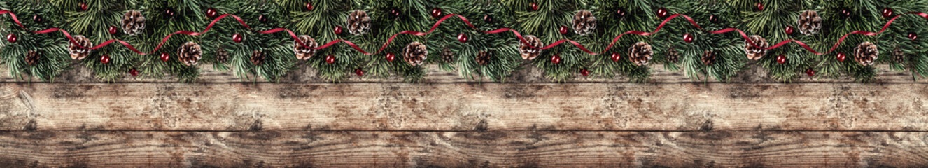 Creative layout frame made of Christmas fir branches, pine cones and red decoration on wooden background. Xmas and New Year theme. Flat lay, top view, wide composition