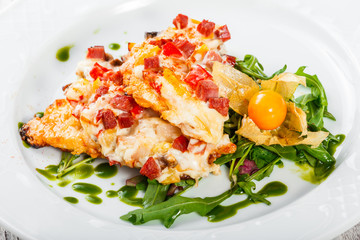 Grilled chicken steaks with cheese, vegetables, ham and salad from arugula, physalis  on wooden background. Hot Meat Dishes. Top view, flat lay