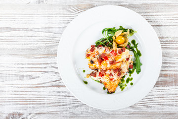 Grilled chicken steaks with cheese, vegetables, ham and salad from arugula, physalis  on wooden background. Hot Meat Dishes. Top view, flat lay