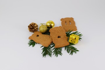 Spekulatius-Plätzchen mit Tannenzweigen, Tannenzapfen und goldenen Christbaumkugeln vor weißem...
