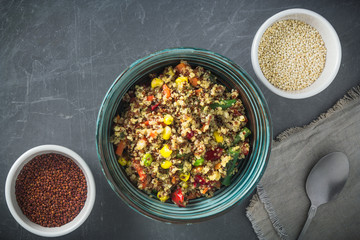 Quinoa salad bowl with various vegetables: green beans, carrot, corn, bell pepper, peas and two bowls with red and white quinoa seeds on grey background. Top view, copy space.