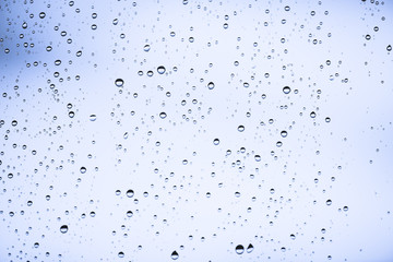 Dirty window glass with drops of rain. Atmospheric blue light background with raindrops. Droplets and stains close up. Detailed transparent texture in macro with copy space. Rainy weather.