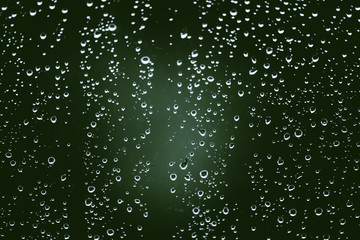 Obraz premium Dirty window glass with drops of rain. Atmospheric green background with raindrops. Droplets and stains close up. Detailed transparent texture in macro with copy space. Rainy weather.