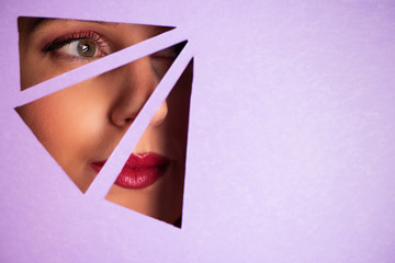 Girl with bright eyes make up looks through hole in violet paper. Business card of artist, beauty...