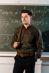 serious male teacher in formal wear holding wooden pointer in front of chalkboard with equations