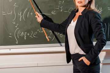 cropped view of female teacher with wooden pointer explaining mathematical equations in classroom