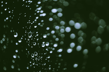 Dirty window glass with drops of rain. Atmospheric green background with raindrops in bokeh. Droplets and stains close up. Detailed transparent texture in macro with copy space. Rainy weather.