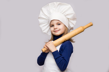 Children cook. Happy little girl in chef uniform holds rolling pin isolated on white background.