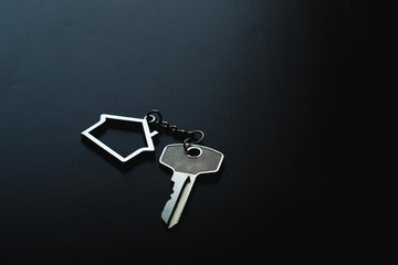Home key with house keyring on black wood table in dark tone, real estate concept