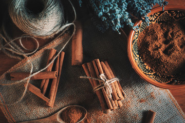 Ground cinnamon, cinnamon sticks, tied with jute rope on old straw bag background in rustic style