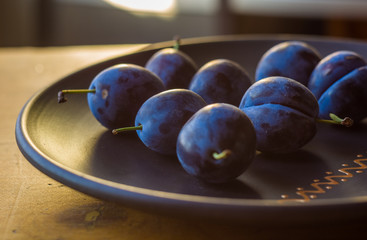 juicy blue plums in ceramic plate on wooden background