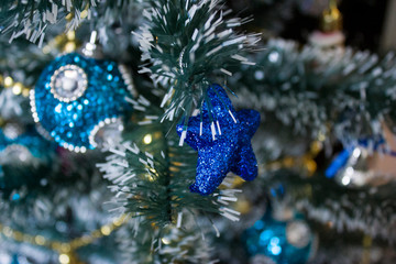brilliant, in sparkles, blue five-pointed star, hung on a branch of an artificial Christmas tree next to other silver toys