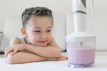 The child observes how the cocktail is made in the mixer. The girl looks like a blender mixes berries, fruit and milk.