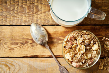 Healthy morning breakfast bowl full of organic granola with a spoon and a jug of milk on an old wooden table