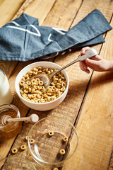 Kids hand holding bowl with healthy breakfast with flakes honey milk and honey dipper on old wooden table