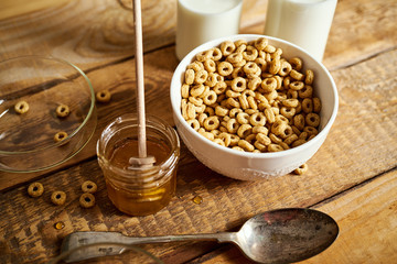 Healthy morning breakfast bowl full of honey flakes with honey dipper and milk on an old wooden table