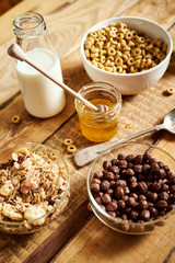 Healthy morning breakfast with different types of breakfast cereals with a spoon, honey and milk on an old wooden table