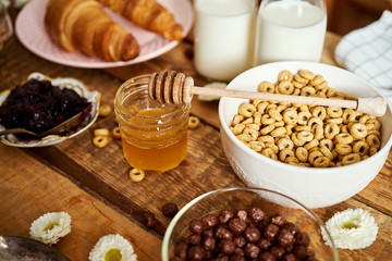 Healthy morning breakfast with different types of breakfast cereal with honey marmalade croissants and milk on old wooden table