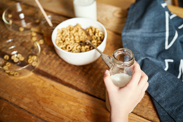 Kids hand holding bowl with healthy breakfast with flakes honey milk and honey dipper on old wooden table